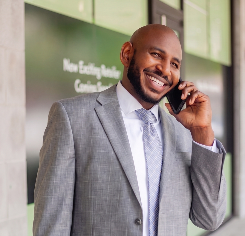 Smiling man in a gray suit talking on a cellphone outside a building