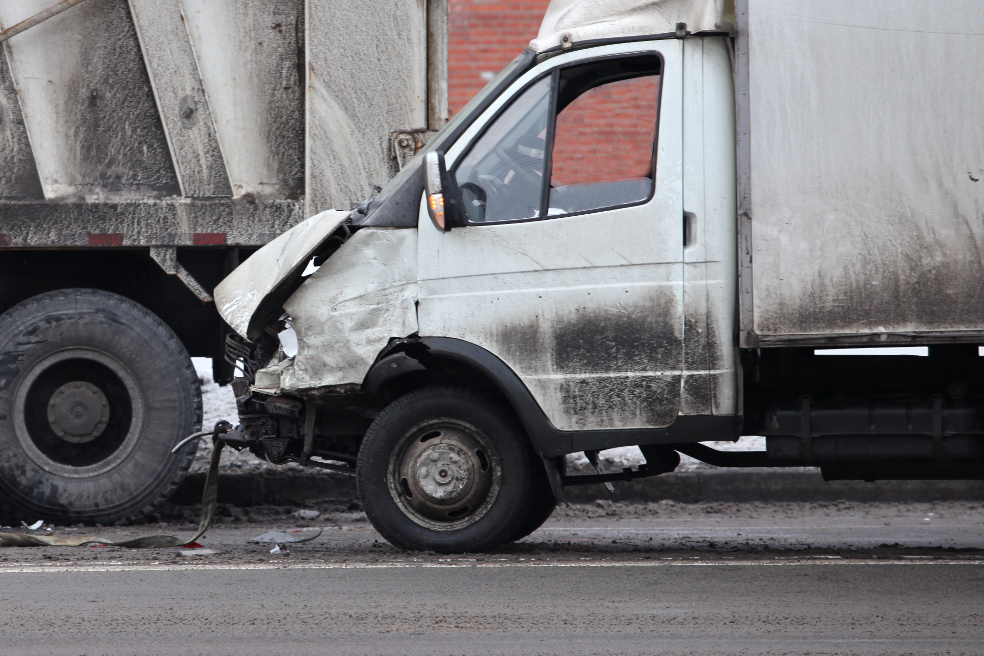 Damaged white van with crumpled front end after a collision with a large truck on a road