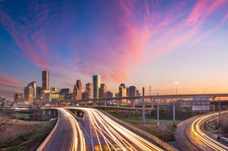 City skyline at dusk with glowing highway light trails and pink clouds