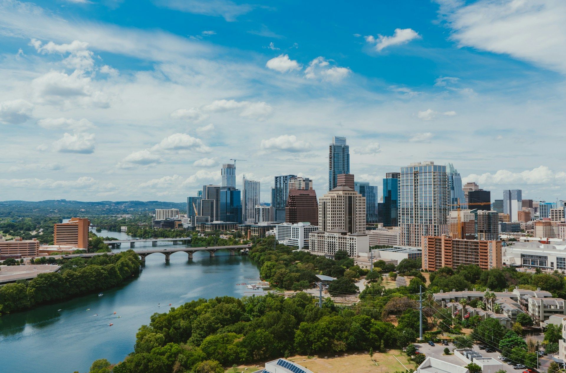 City skyline beside a river under a blue sky with scattered clouds