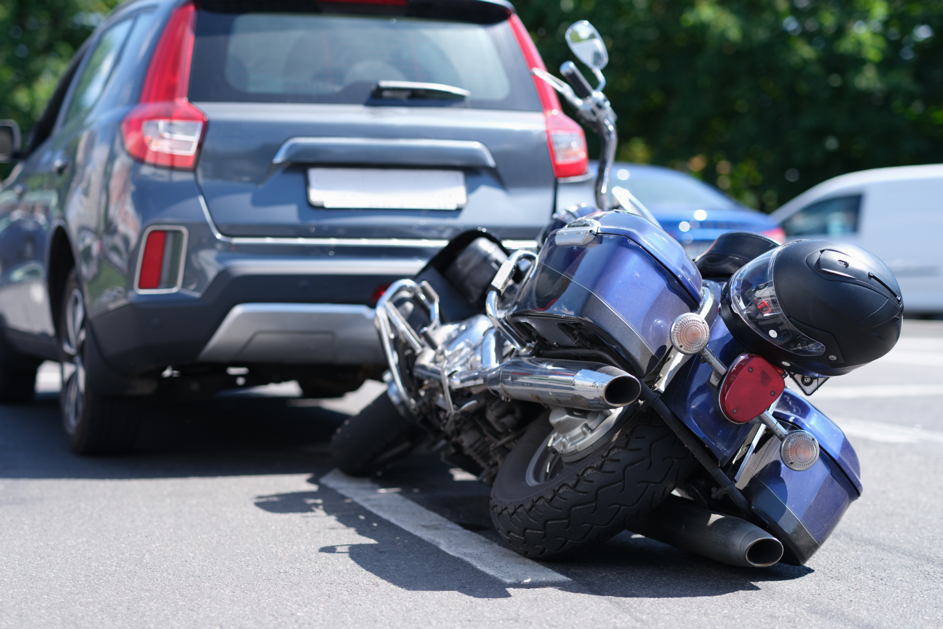 Motorcycle lying on its side behind a gray SUV after a road collision, with debris on the pavement