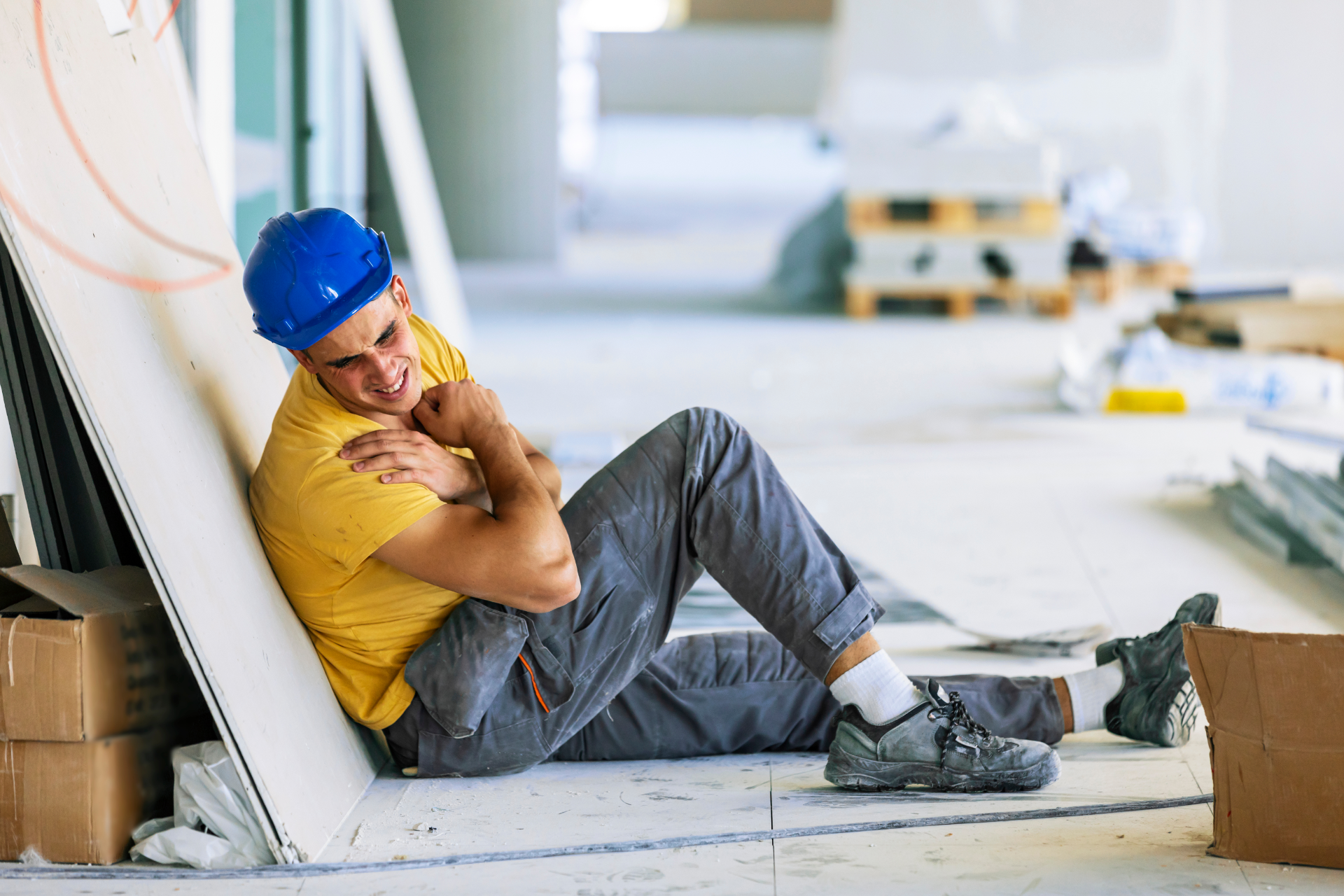 Construction worker in a blue hard hat and yellow shirt sitting on a floor, smiling and resting