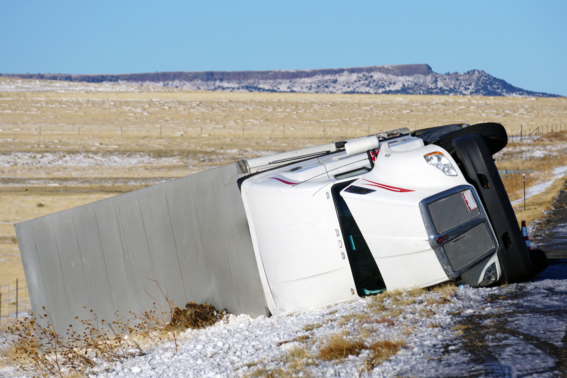 Overturned white truck beside a roadside barrier in a snowy field