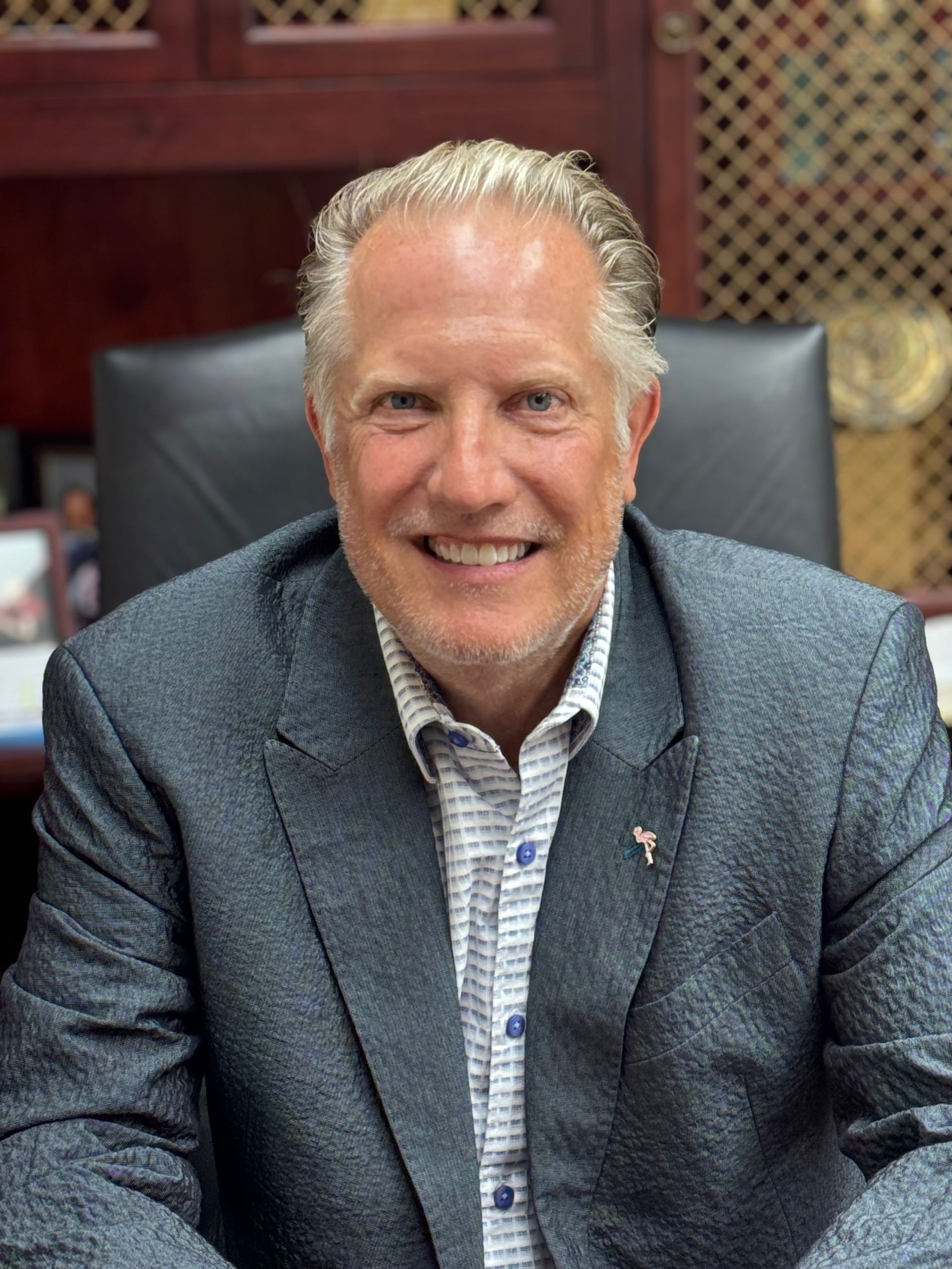 A man in a suit is sitting in a chair and smiling.