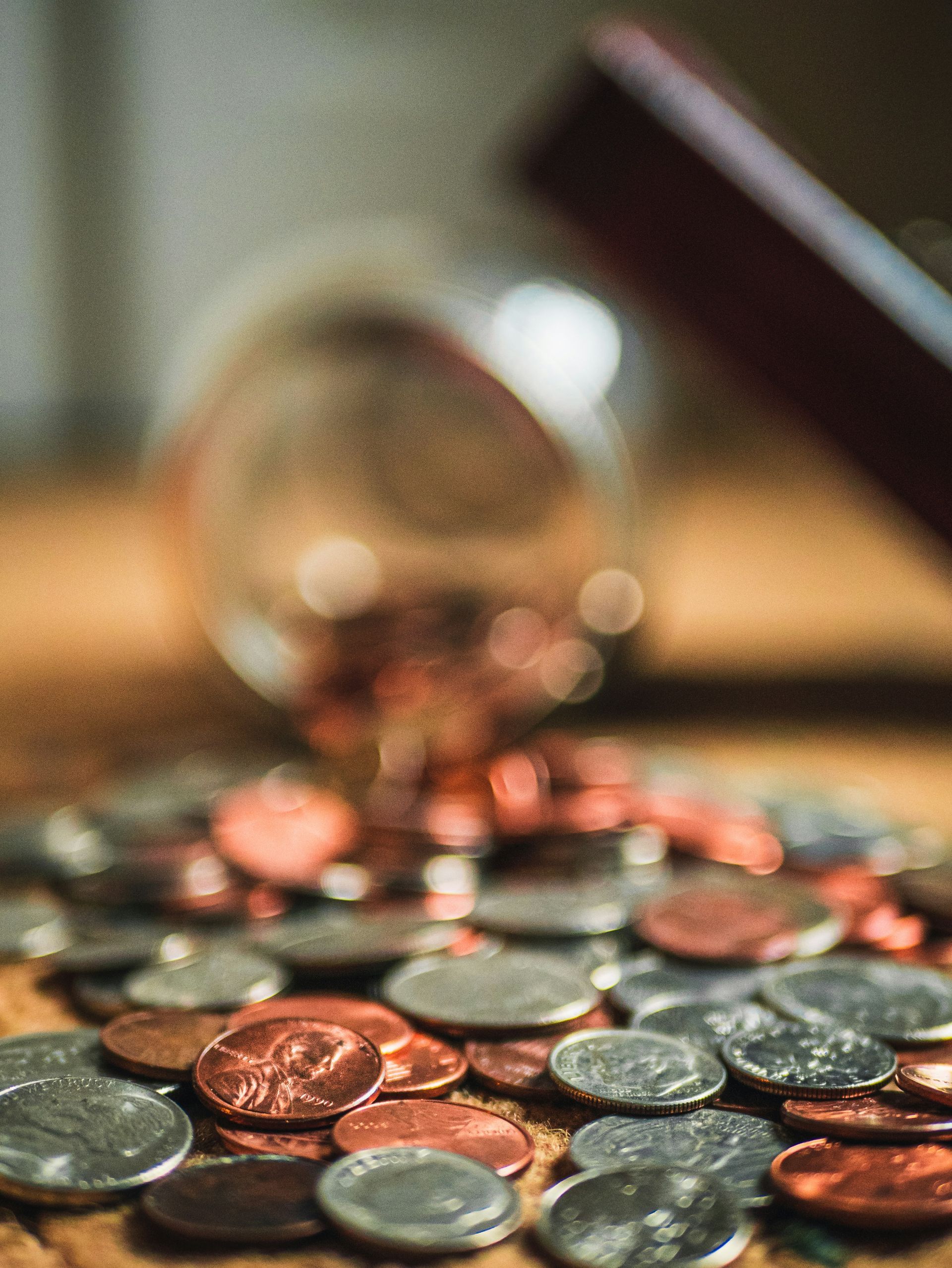 A glass jar filled with coins is sitting on top of a pile of coins on a table.