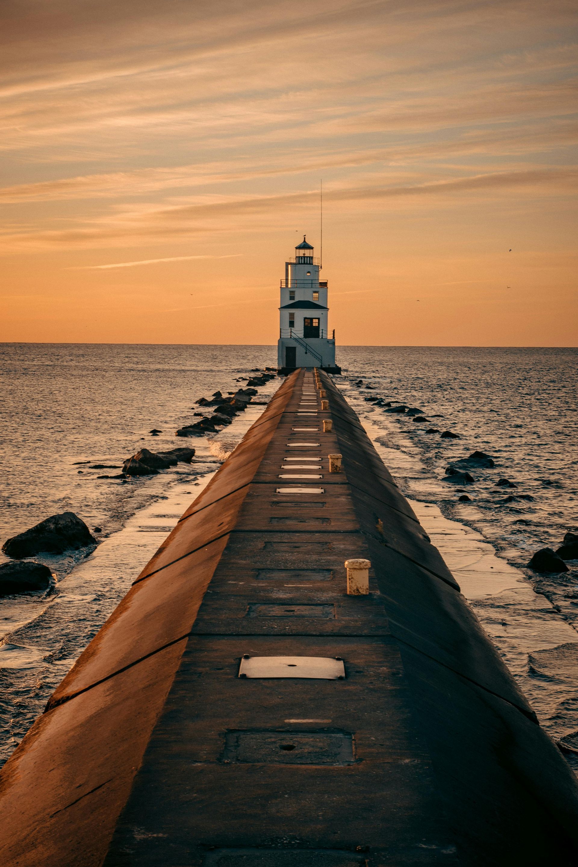 A lighthouse is at the end of a pier in the middle of the ocean.