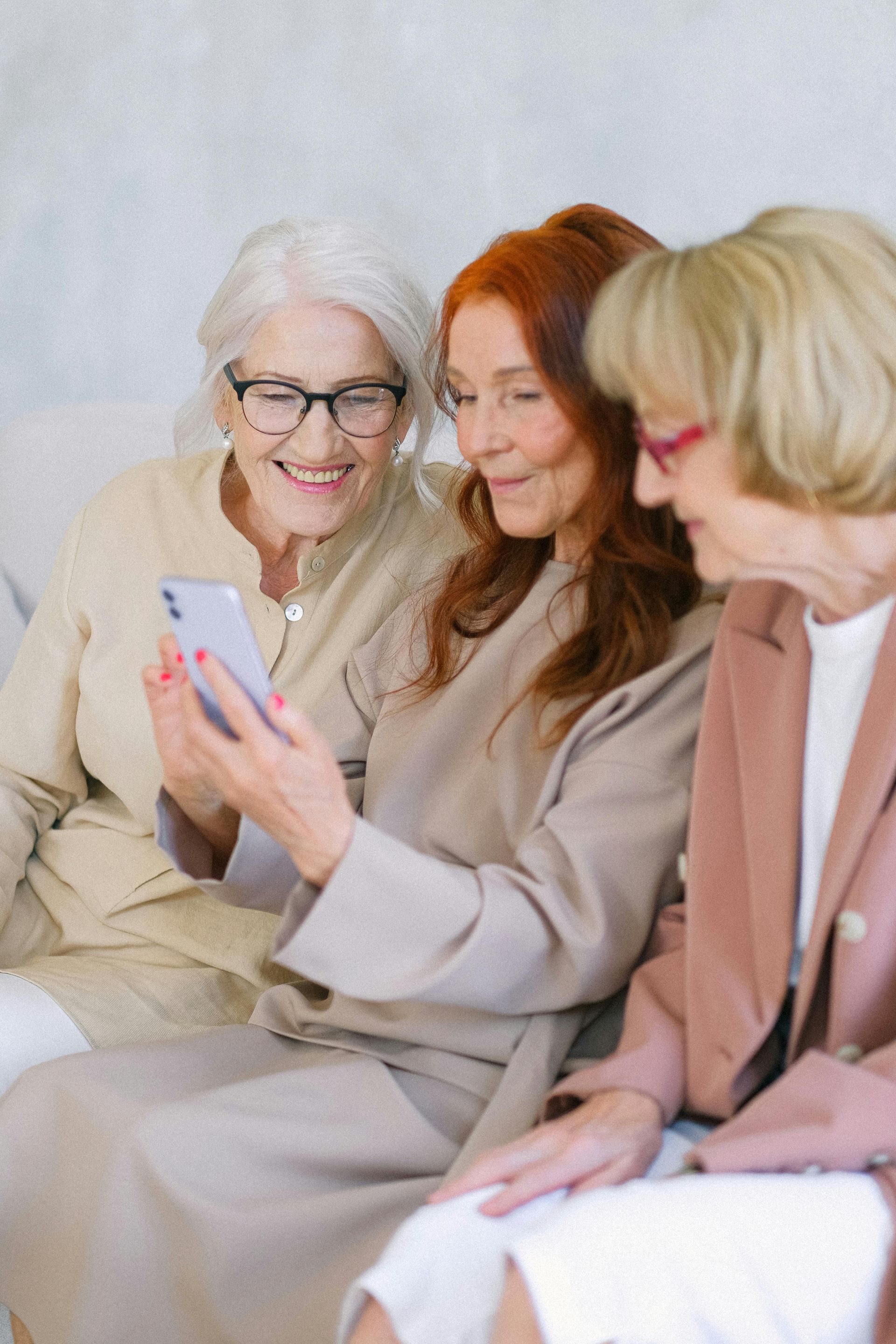 Three older women are sitting on a couch looking at a cell phone.
