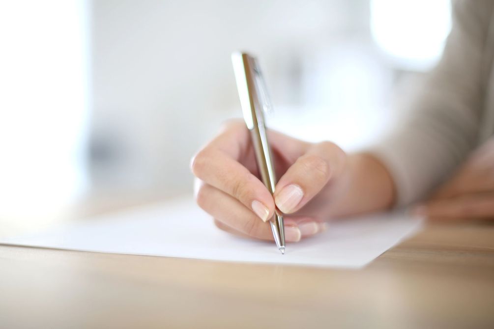 Una mano che tiene una penna e scrive su un foglio bianco alla scrivania