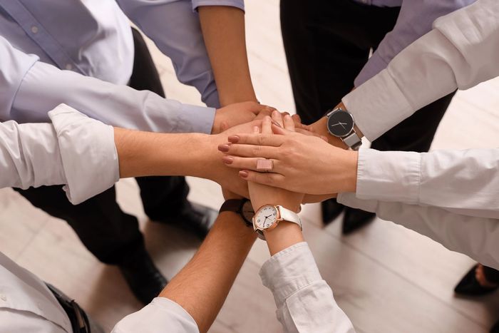 I membri del team in camicia bianca mettono le mani una sopra l’altra durante una riunione di gruppo in ufficio