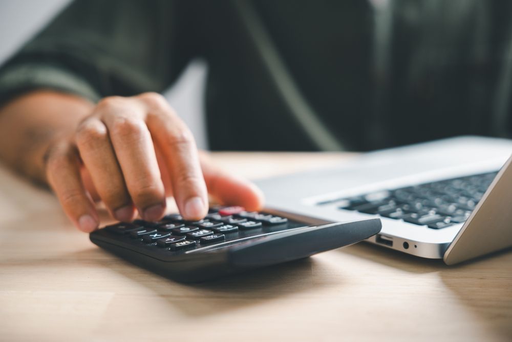 A person is using a calculator in front of a laptop computer.