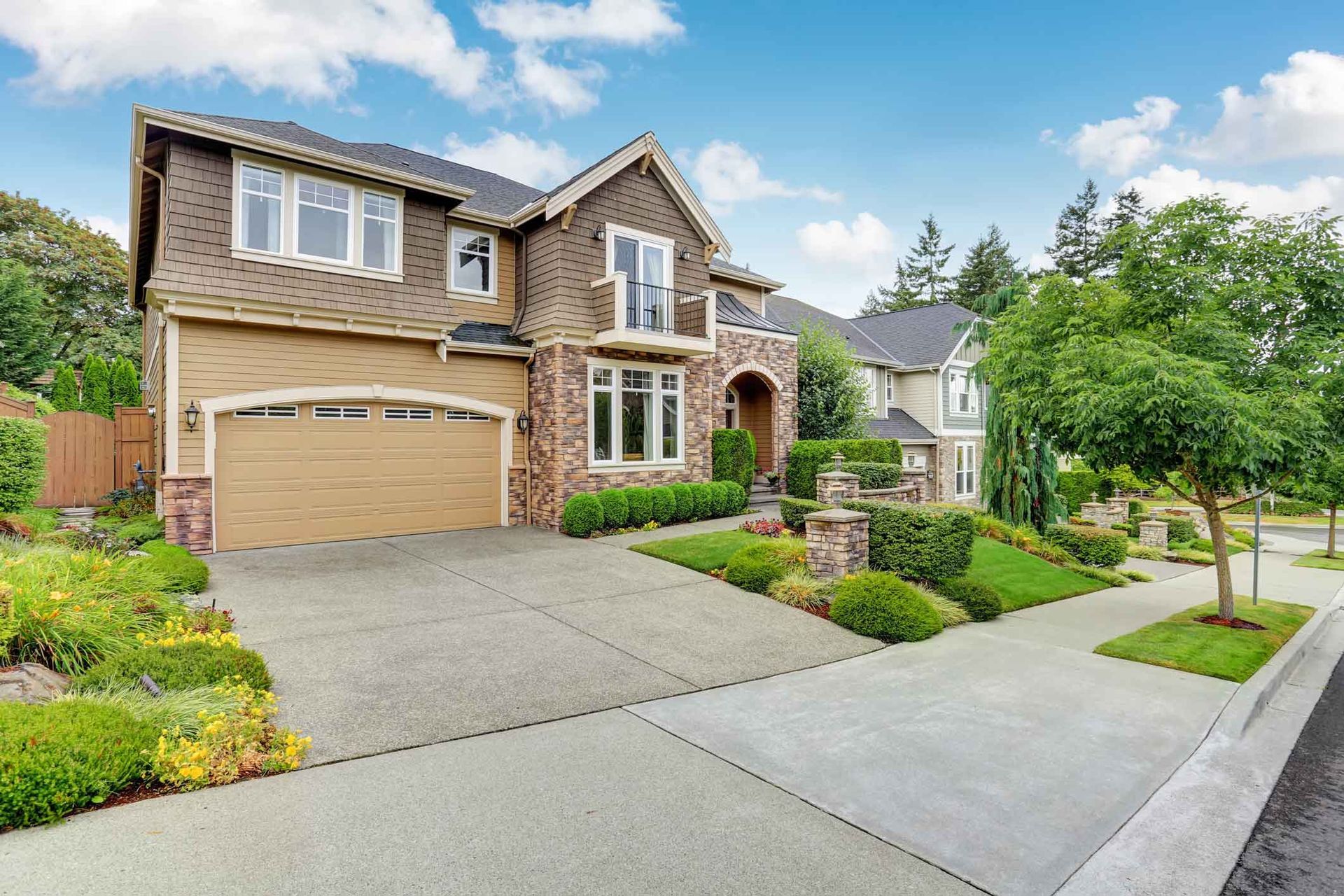 Suburban brick house with a two-car garage, landscaped front yard, and driveway on a sunny day