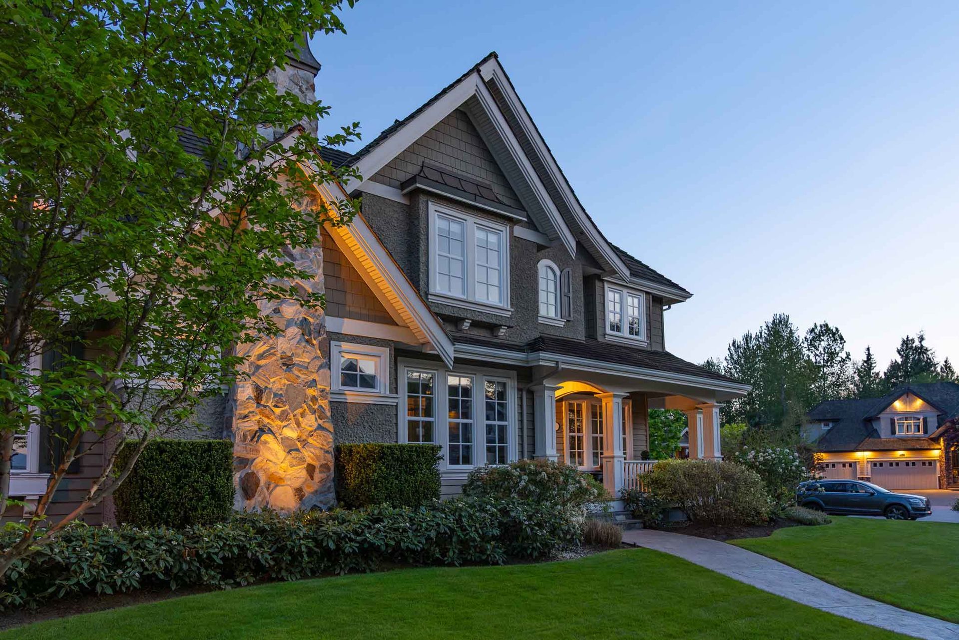 Large two-story suburban house at dusk with warm porch lights and a manicured lawn