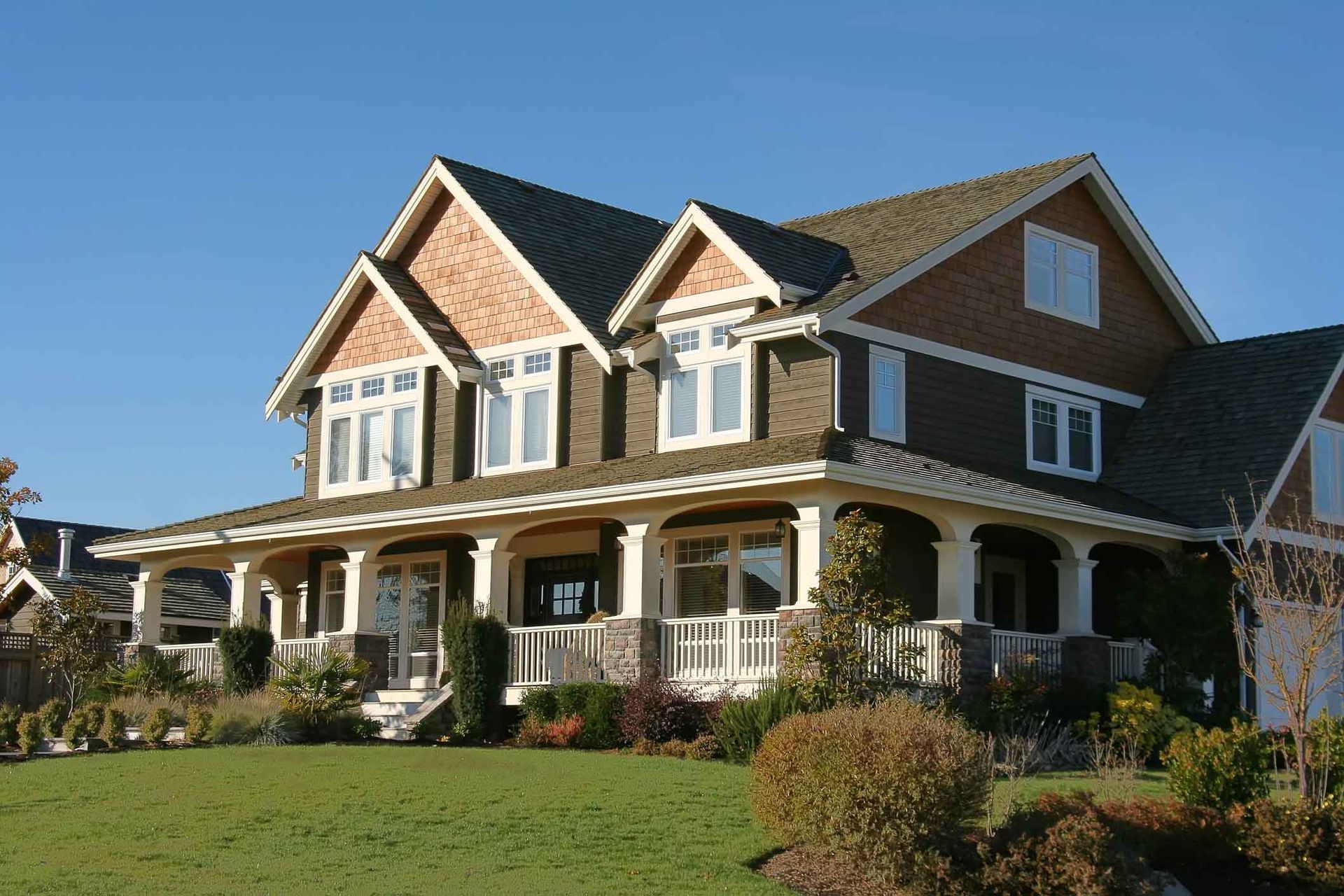 Large two-story suburban house with a porch, gray siding, and white trim on a sunny lawn.