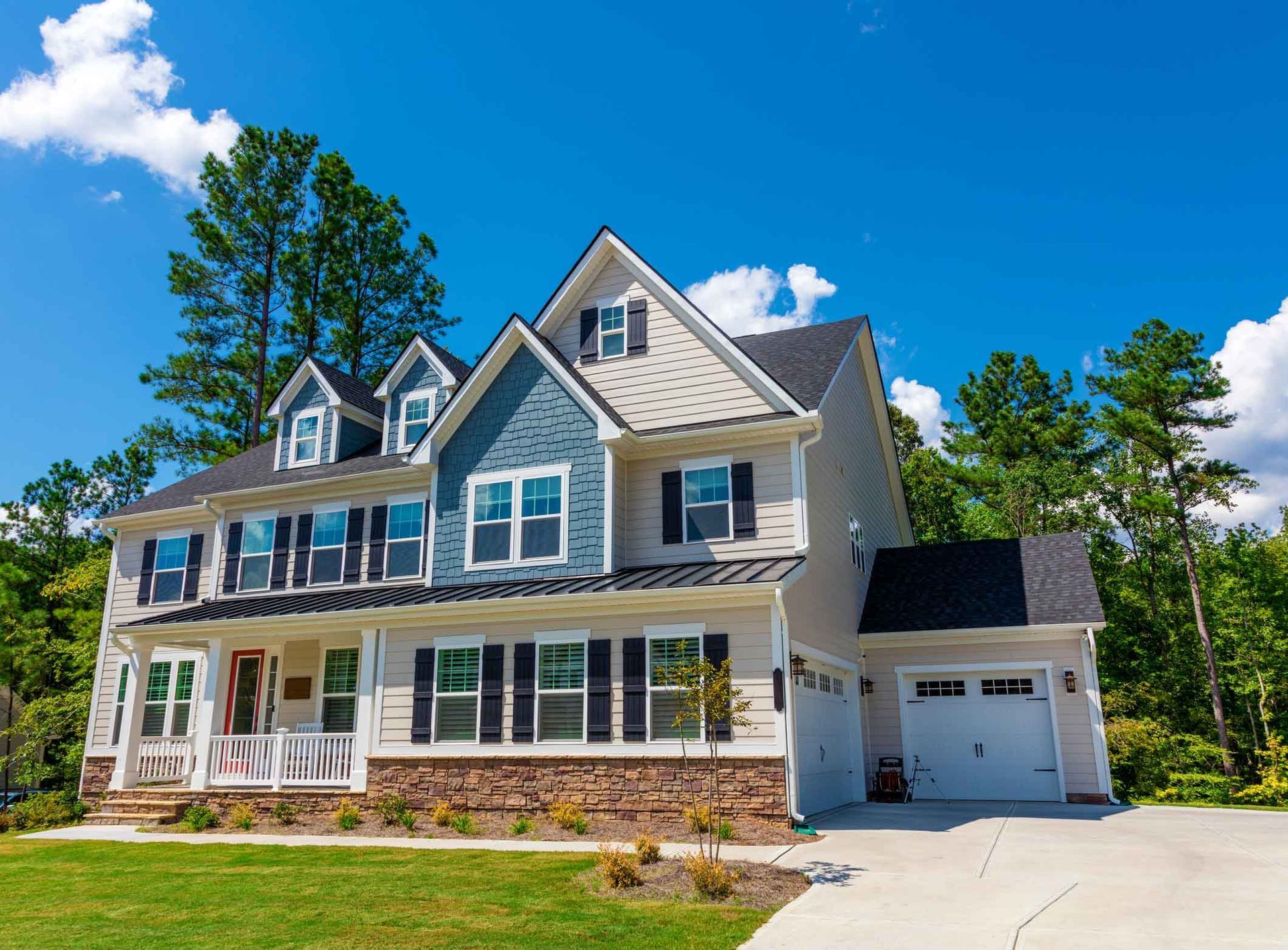 Large gray suburban house with white trim, front porch, and attached garage under a bright blue sky