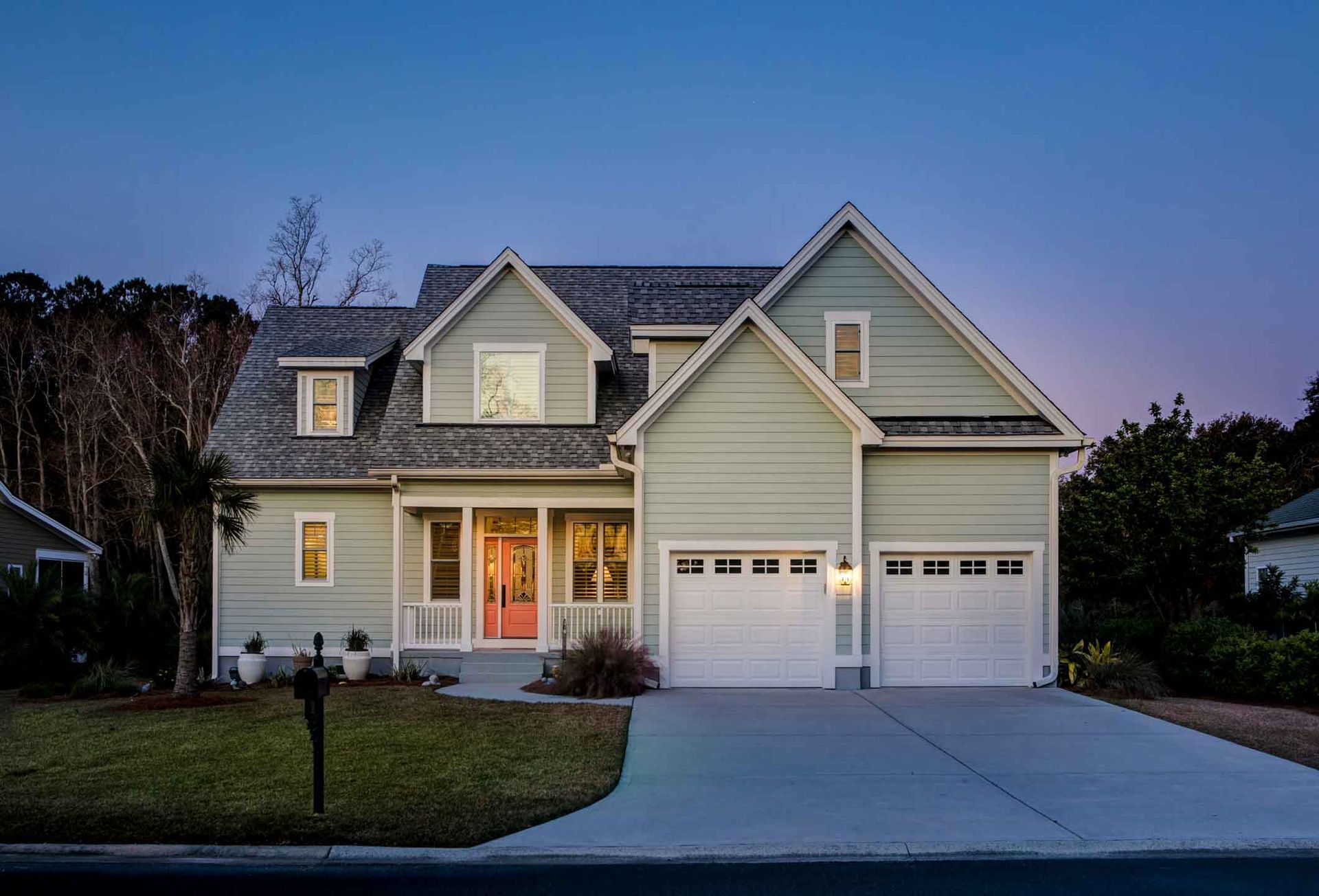 Suburban house at dusk with lit windows, two-car garage, and driveway leading to the front entrance