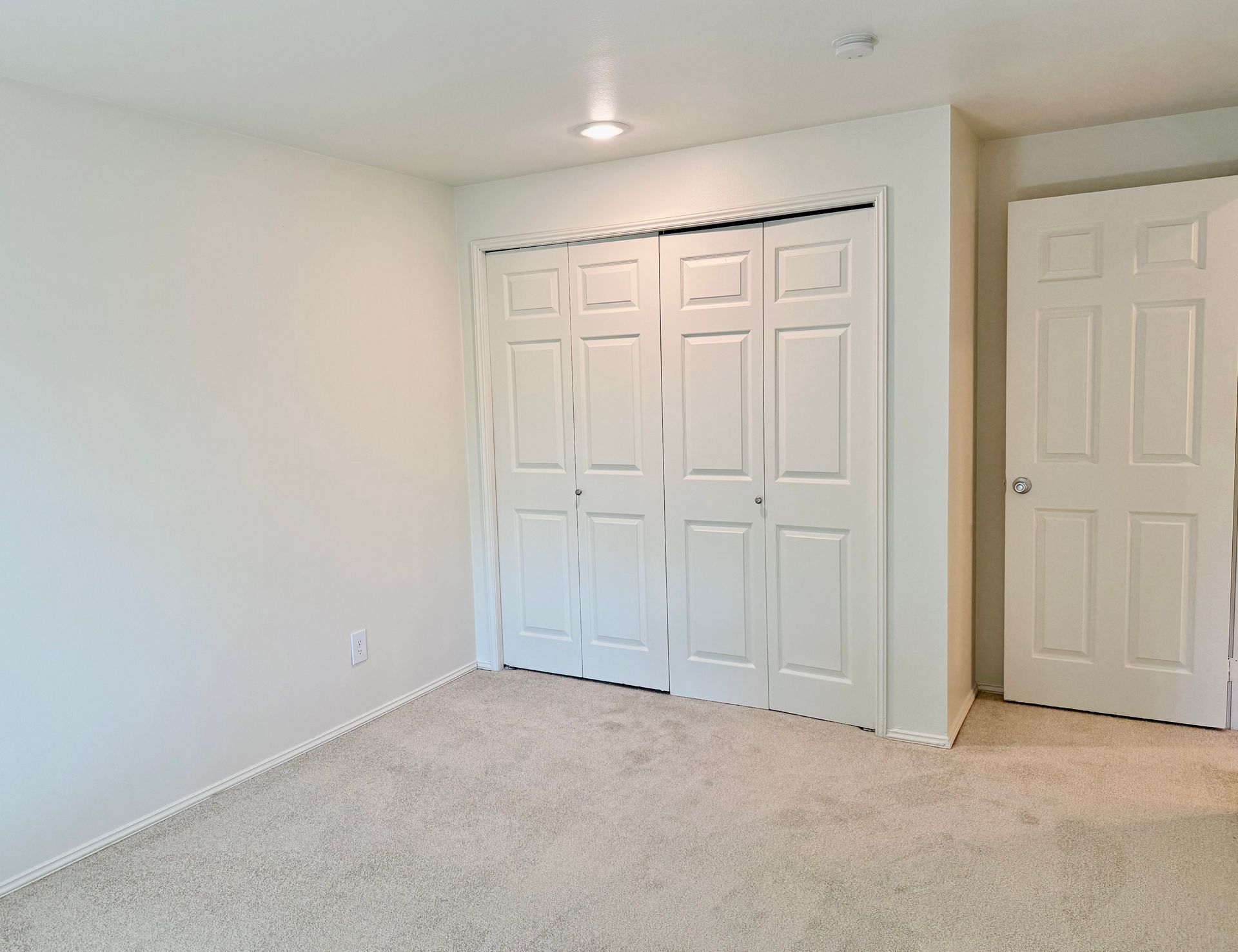 An empty bedroom with white walls and white closet doors.