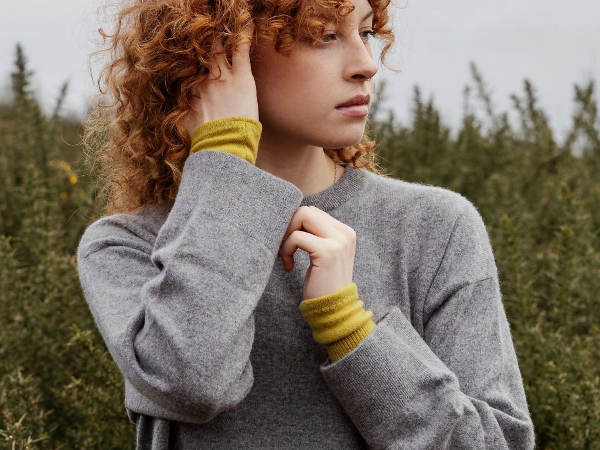 photo of a woman in the Scottish highlands wearing a grey cashmere jumper and mustard yellow cashmere wrist warmers
