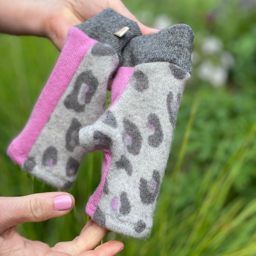 Colourful pair of cashmere fingerless gloves, being held outside in front of a green garden of plants