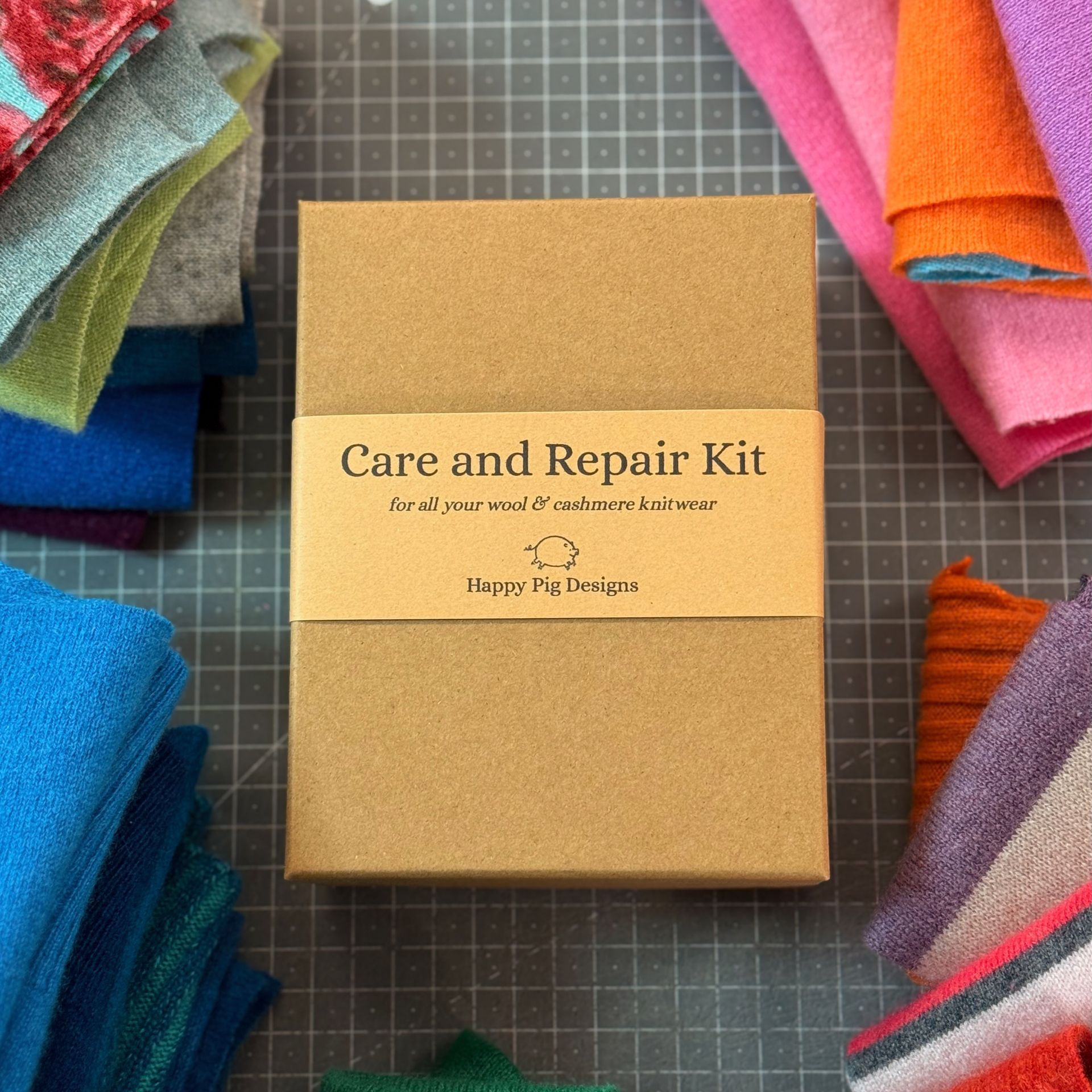 a photo of a cashmere repair kit in a rectangular gift box surrounded by piles of colourful cashmere pieces