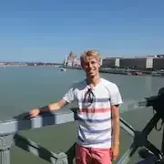 Een jonge man staat op een brug over een watermassa.
