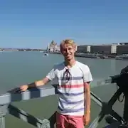 Ein junger Mann steht auf einer Brücke und blickt auf ein Gewässer.