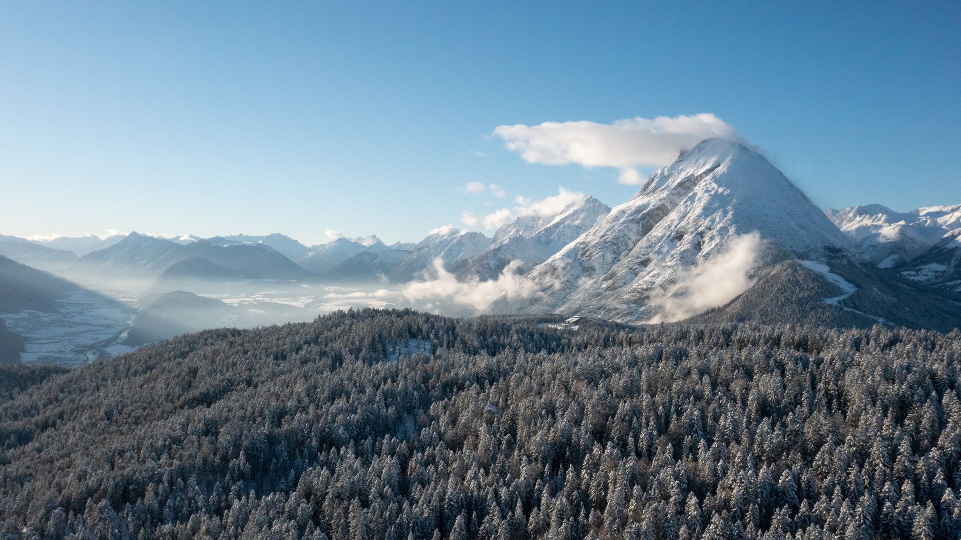 Eine Luftaufnahme einer schneebedeckten Bergkette mit Bäumen im Vordergrund.
