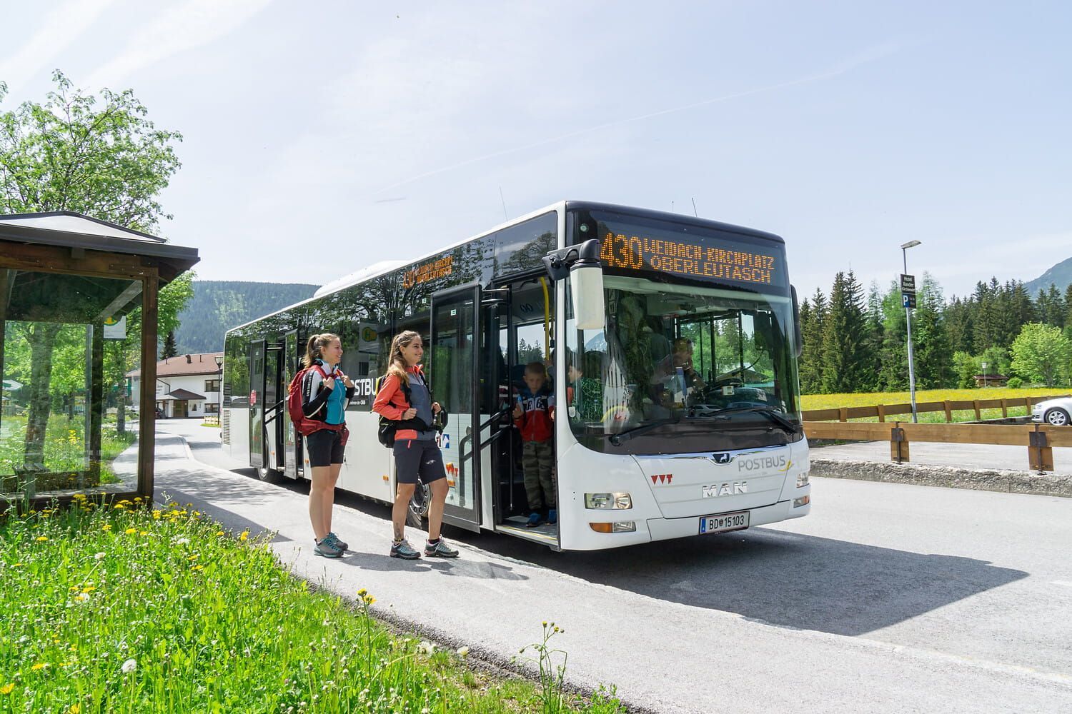 Tour bus stopped at a roadside stop with two people boarding under a sunny sky