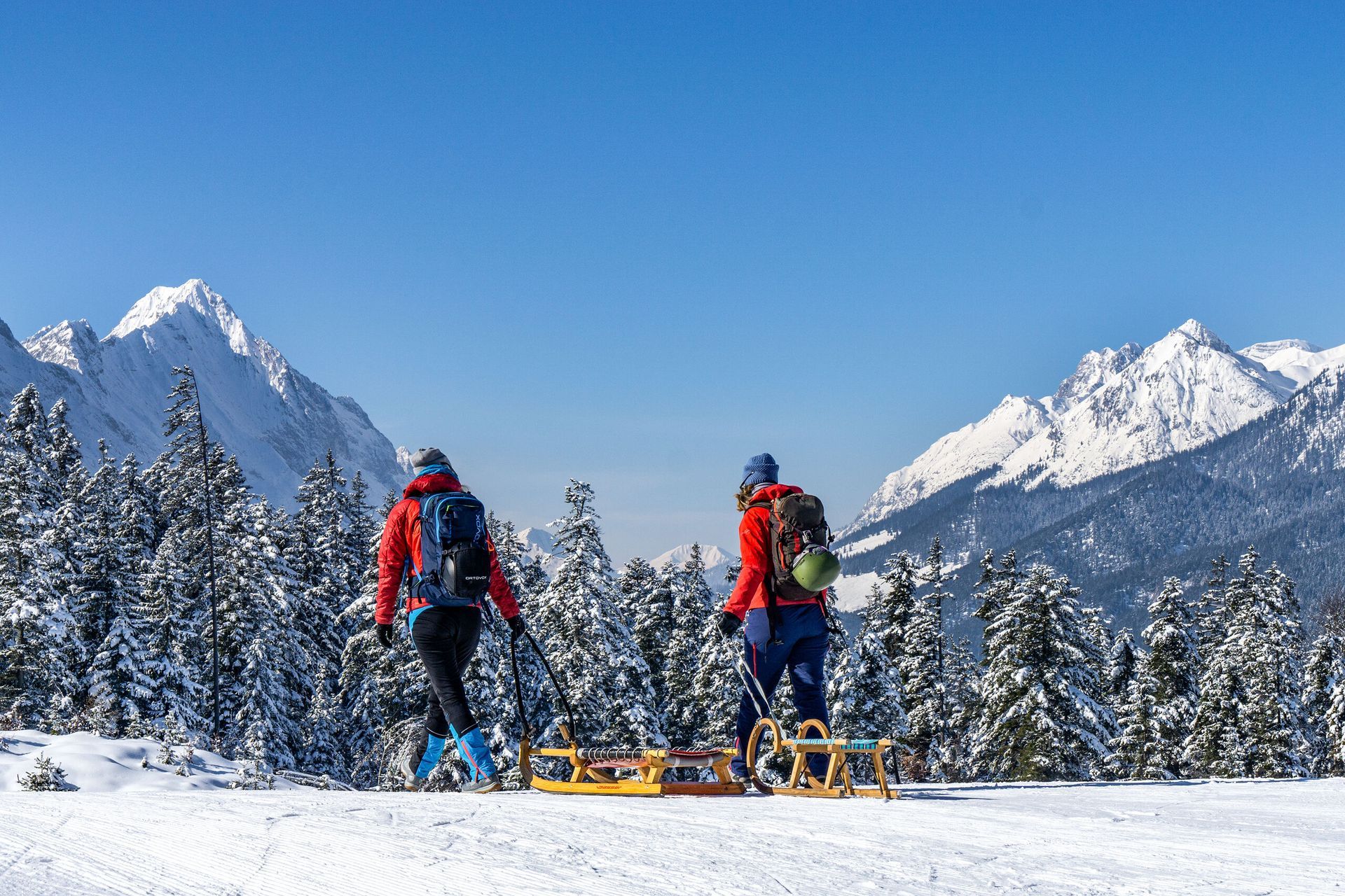 Zwei Personen laufen mit einem Schlitten durch den Schnee.