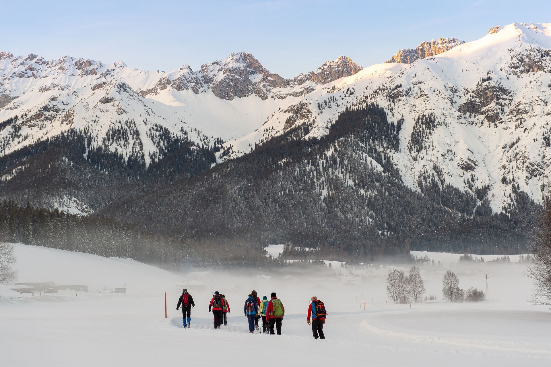Eine Gruppe von Menschen geht durch ein schneebedecktes Feld mit Bergen im Hintergrund