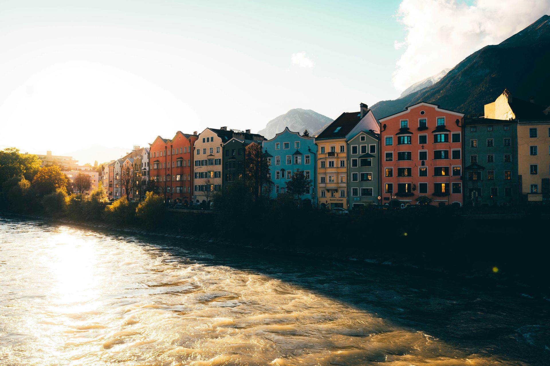 Eine Reihe farbenfroher Gebäude neben einem Fluss mit Bergen im Hintergrund.