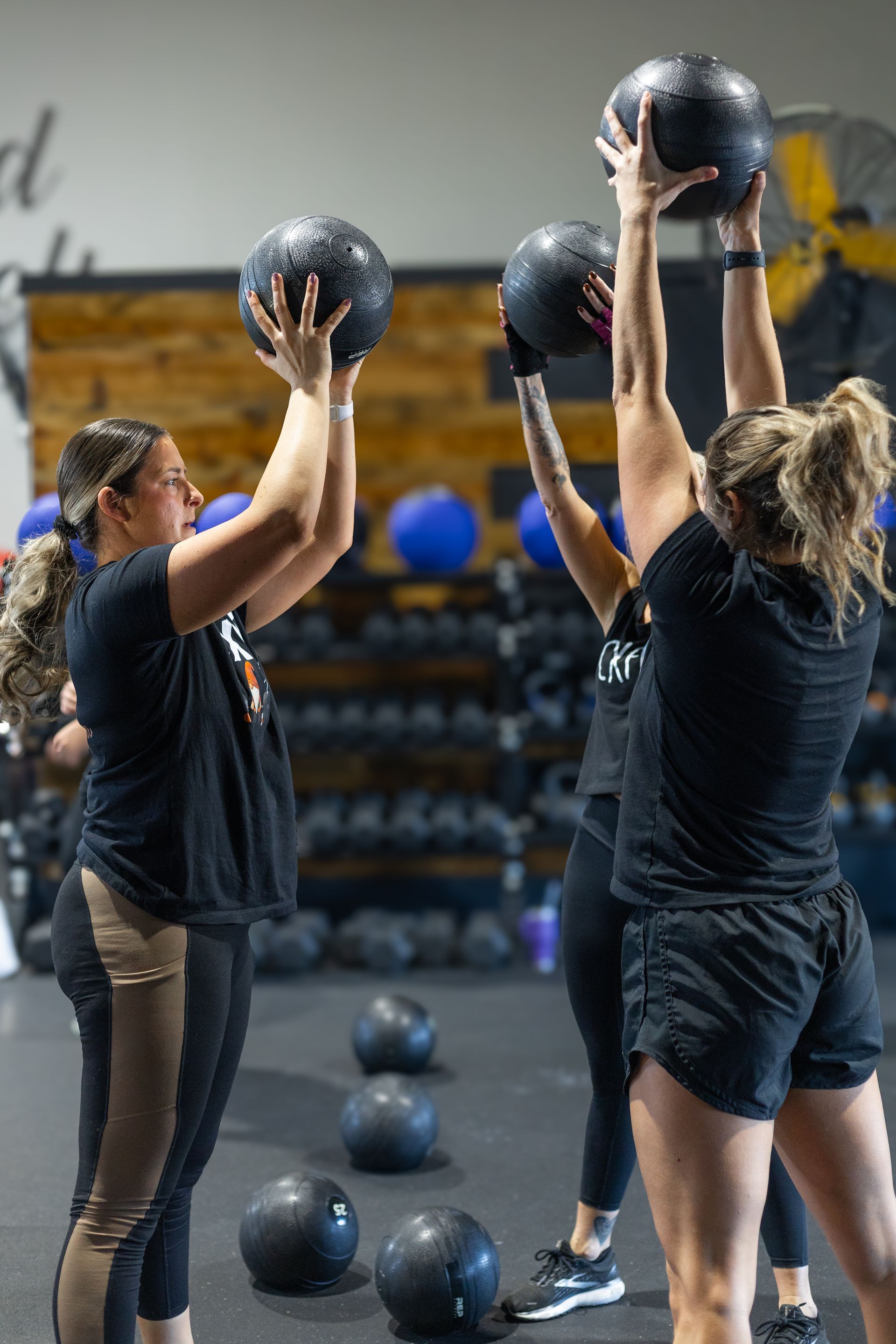 People exercising with medicine balls in a gym, lifting them overhead during a workout class