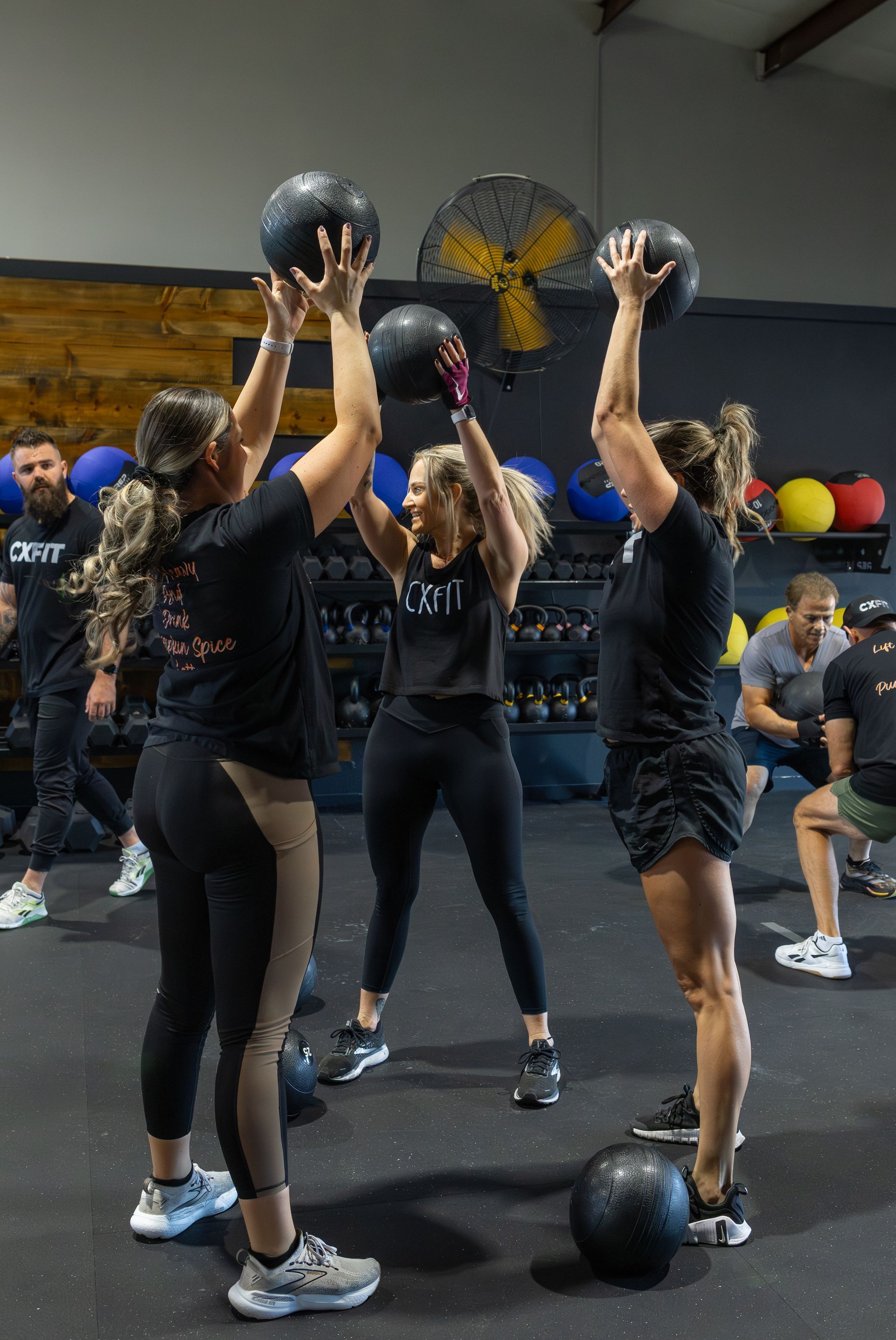 Group exercising with medicine balls in a gym, raising them overhead during a workout class