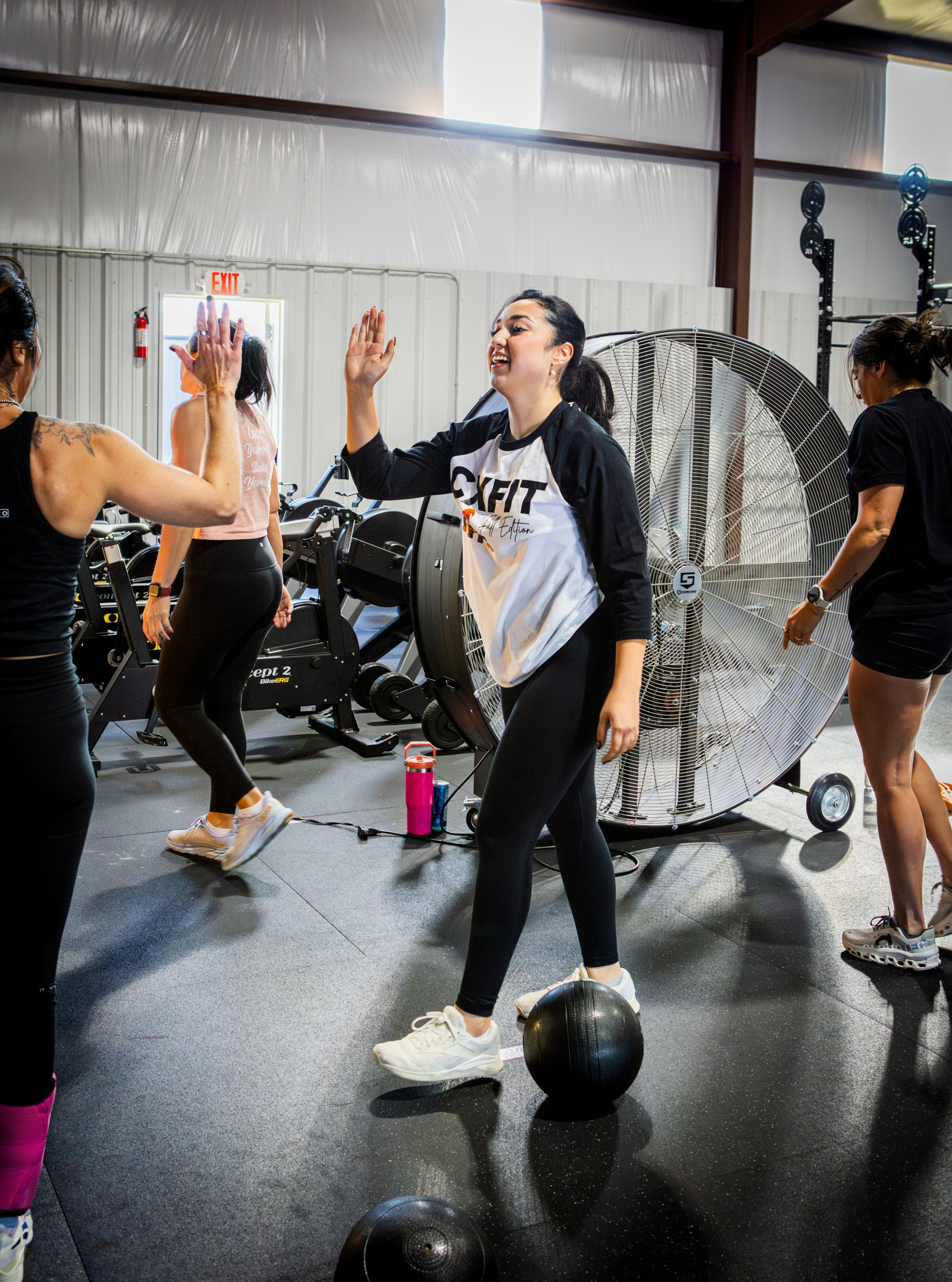 People exercising in a gym, smiling and high-fiving near a medicine ball and exercise equipment.