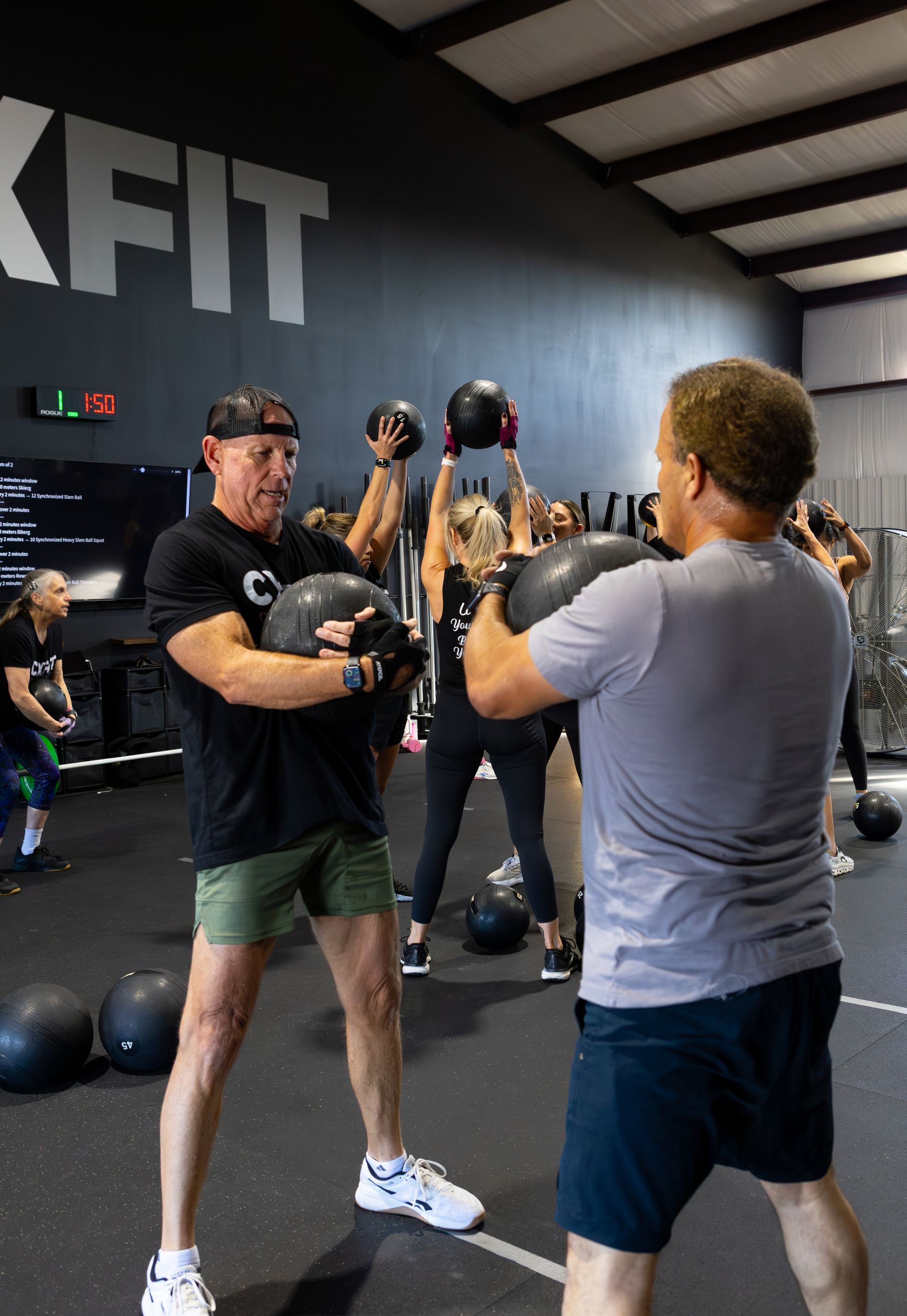 People doing kettlebell exercises in a CrossFit gym, with a coach demonstrating in front of a mirror.