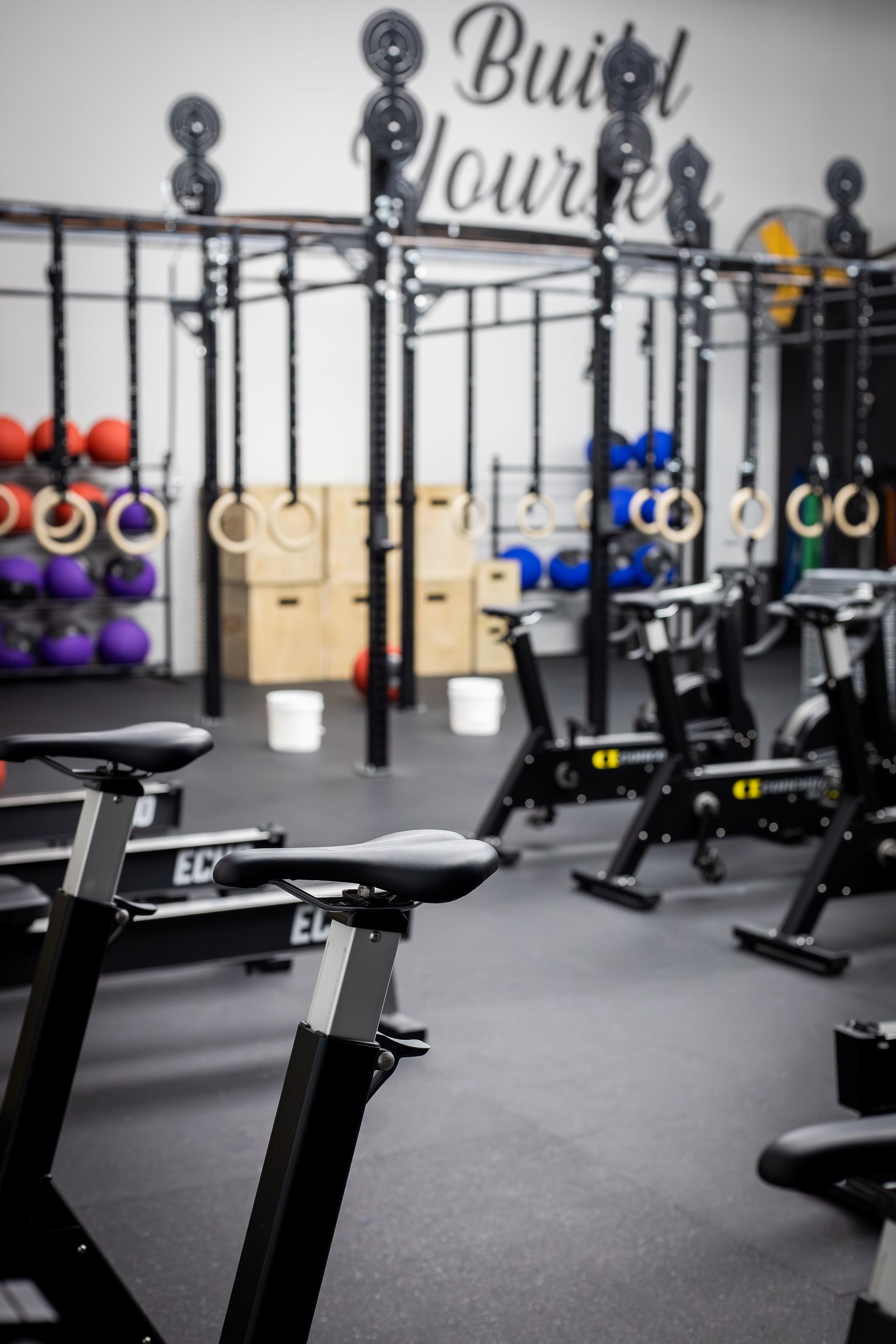 Modern gym with stationary bikes, kettlebells, and wall-mounted equipment racks