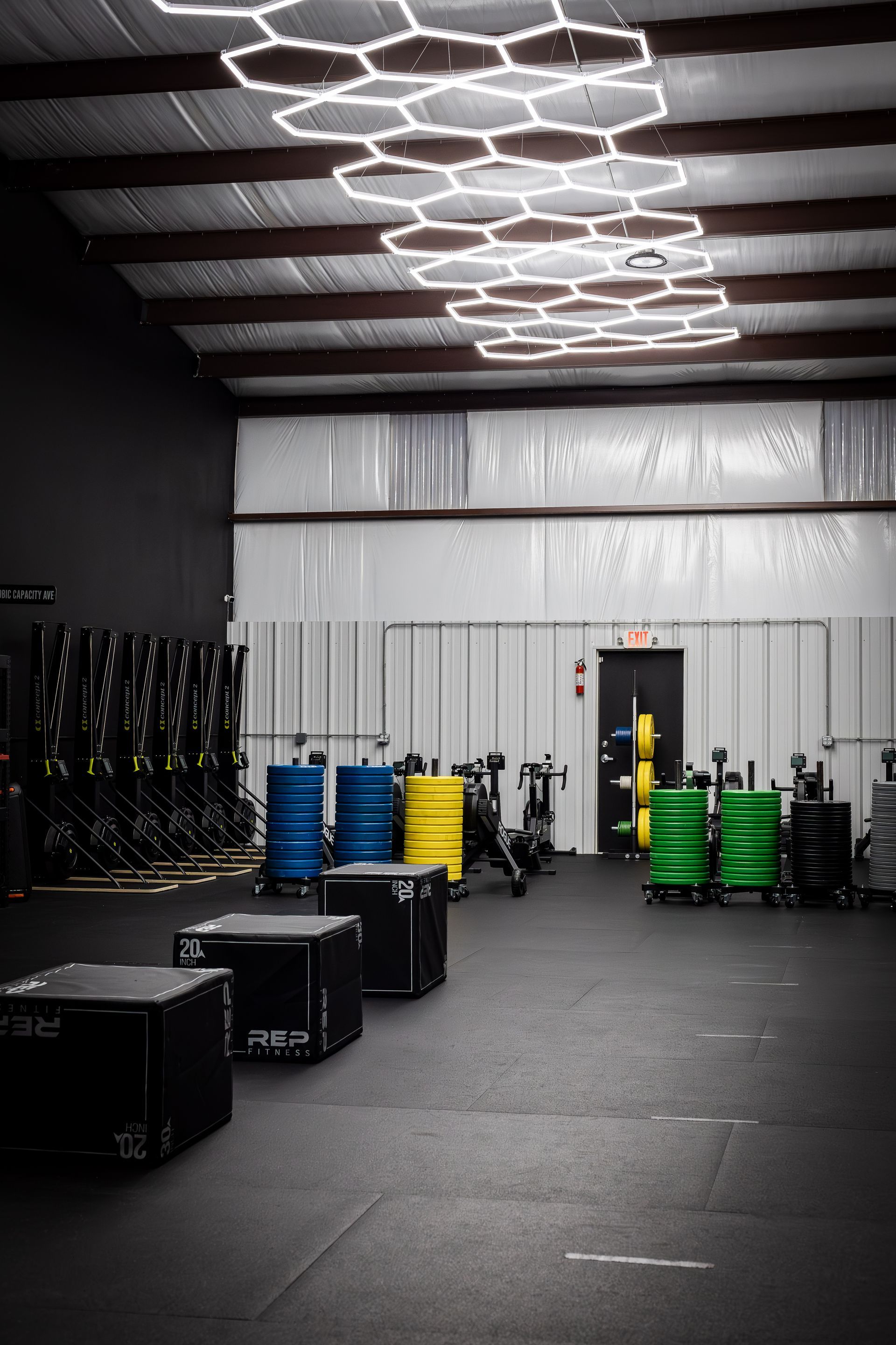 Empty gym interior with barbells, weight plates, and hexagon ceiling lights