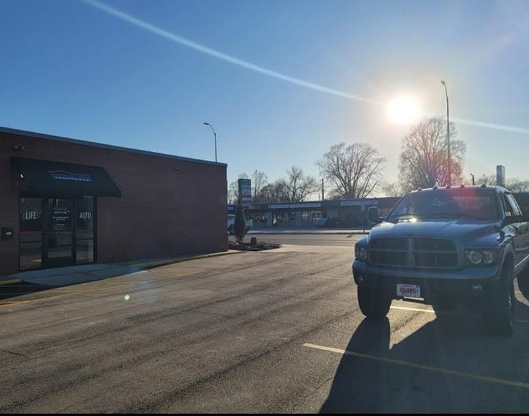 Sunlit parking lot beside a brick building, with a black truck parked at right.