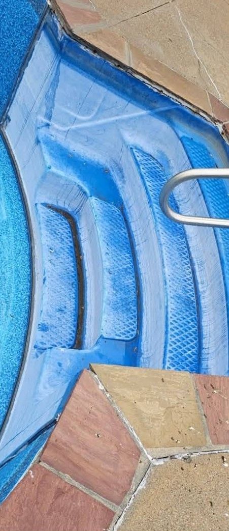 Blue painted curb with stepped concrete edge beside terracotta tiles and a metal ring handle