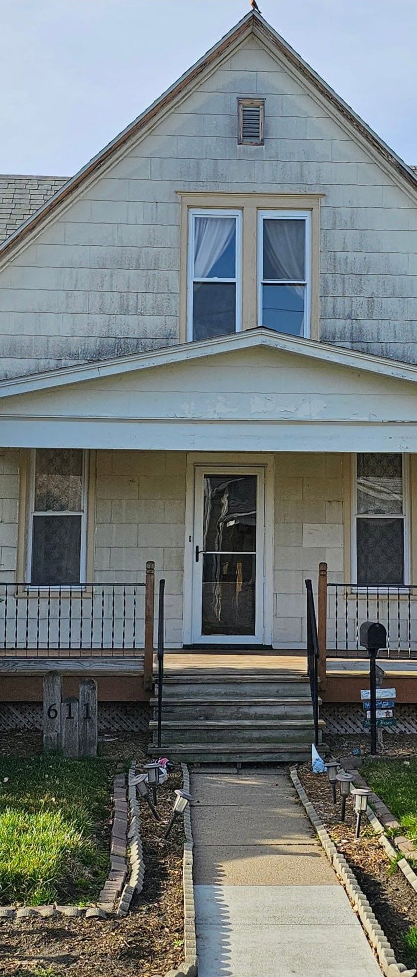 Weathered white house with front porch, steps, and a narrow walkway leading to the entrance