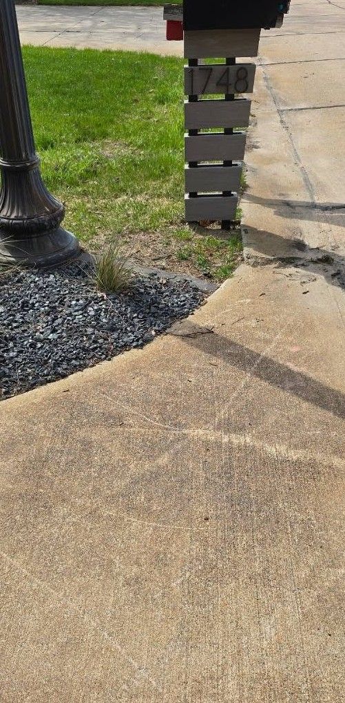 Concrete sidewalk beside a black lamp post and house number sign next to grass and gravel edging