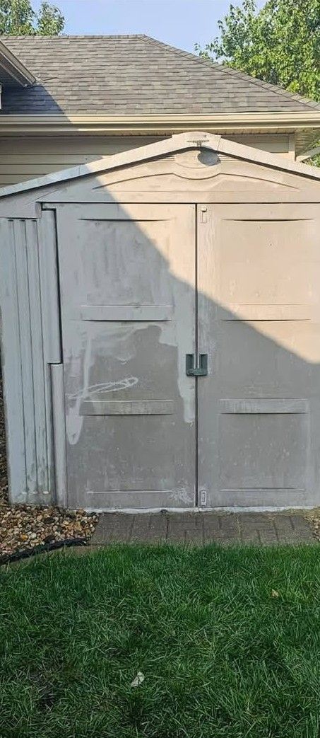 Weathered white shed with double doors in a grassy backyard, casting a diagonal shadow.