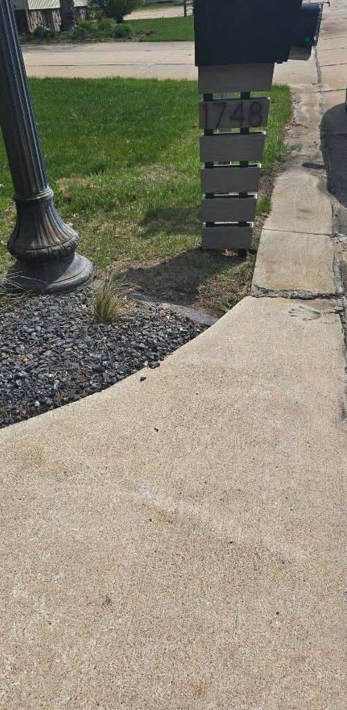 Curved concrete sidewalk beside a black lamp post and stacked stone mailbox pillar with gravel edging