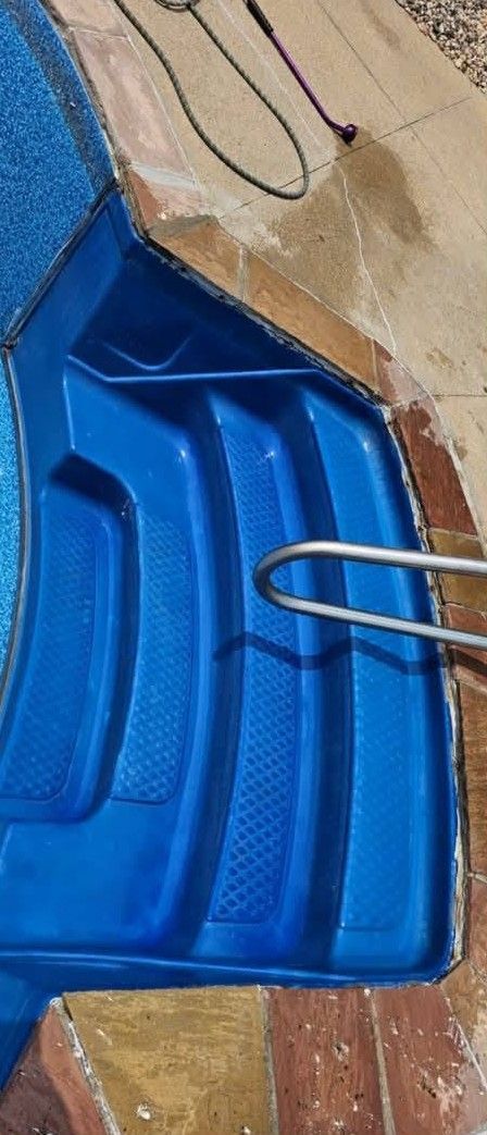 Blue plastic sled leaning against a wall with a metal handle and rope nearby