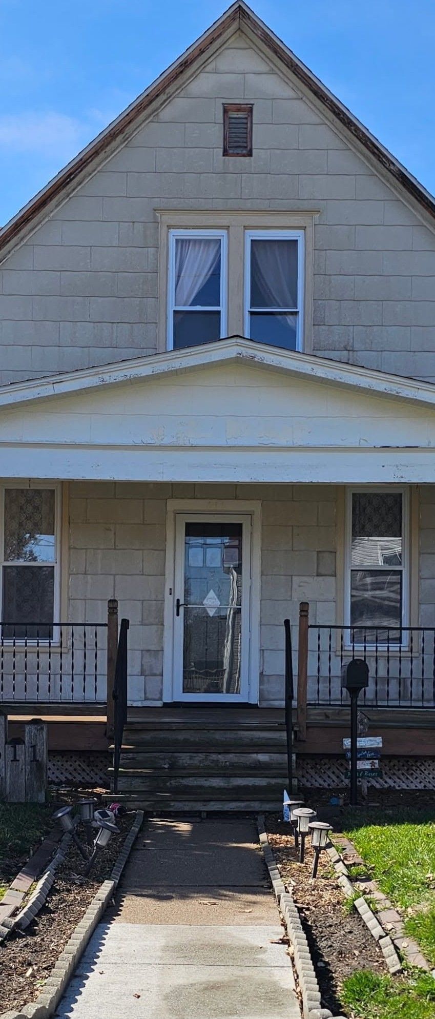 Front view of a beige two-story house with a porch, white trim, and a narrow front walkway