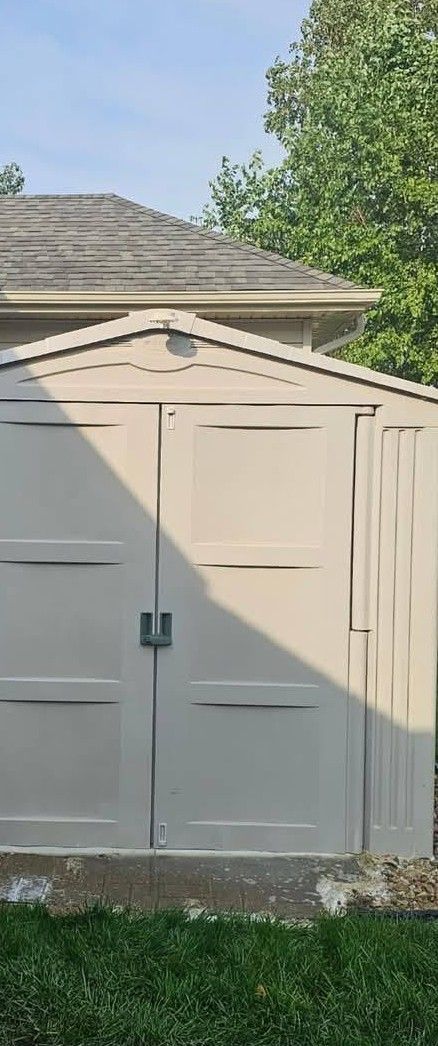 Beige backyard shed with double doors, in front of a house and trees.