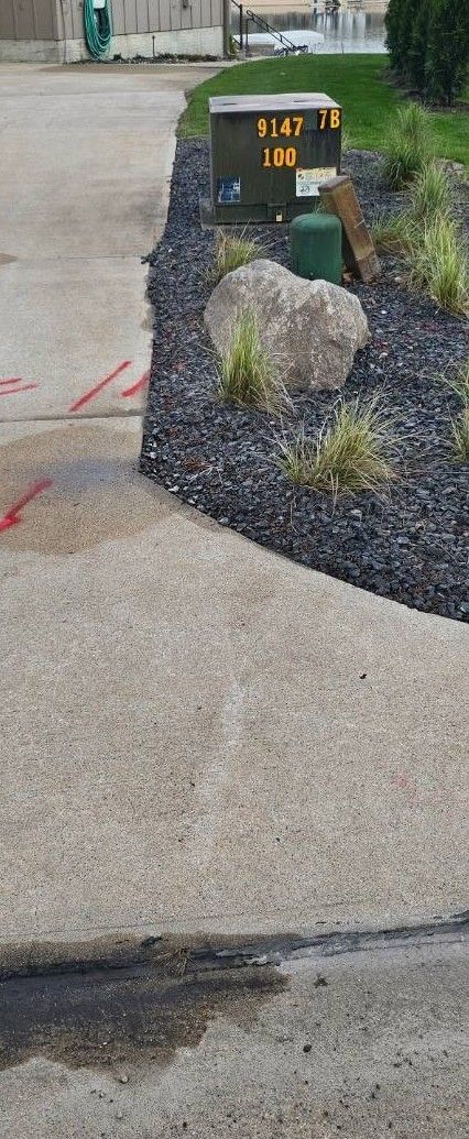 Sidewalk with a green utility box and rocks bordering a gravel path near a curb