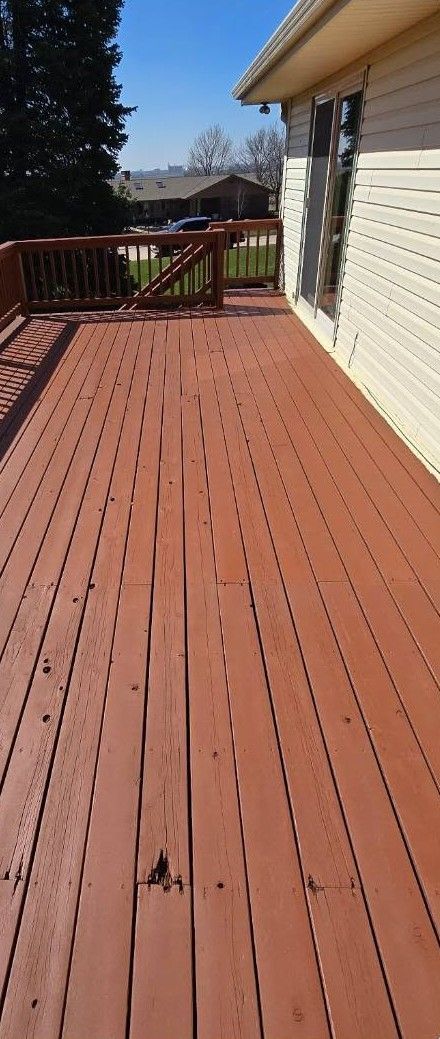 Wooden deck beside a white house, with railing and a bright blue sky beyond.