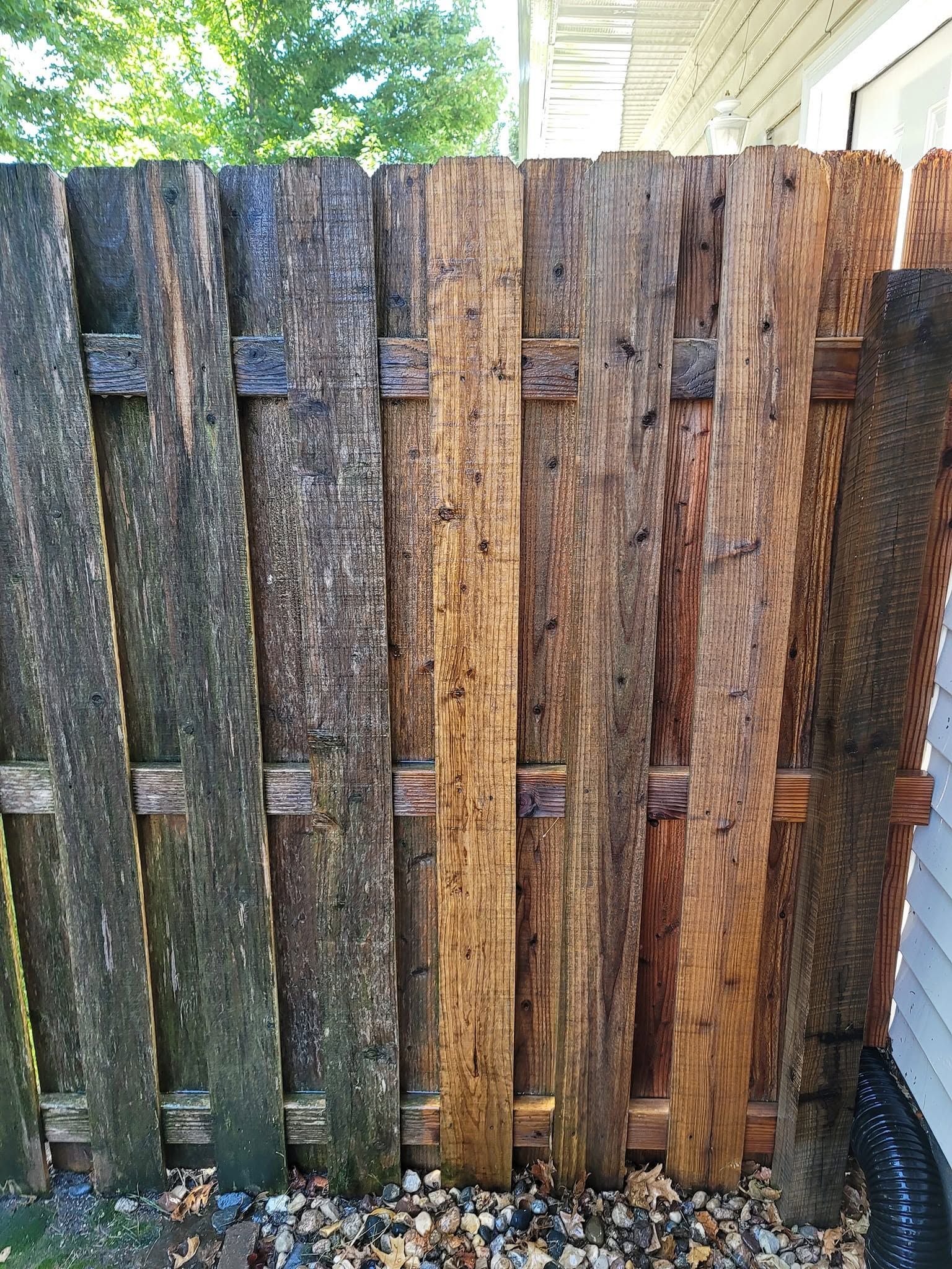 Weathered wooden fence panels in blue-gray, brown, and orange tones beside a house and greenery