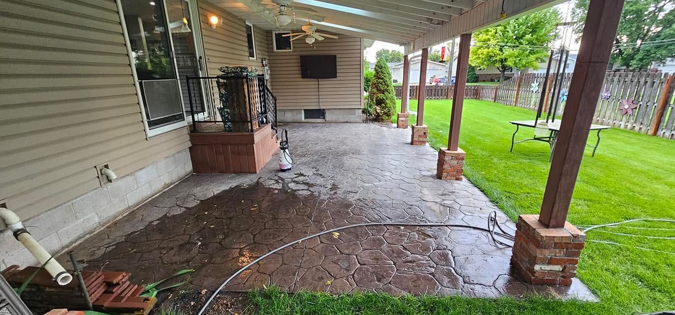 Covered backyard patio with wet concrete floor, brick columns, and green lawn beside the house
