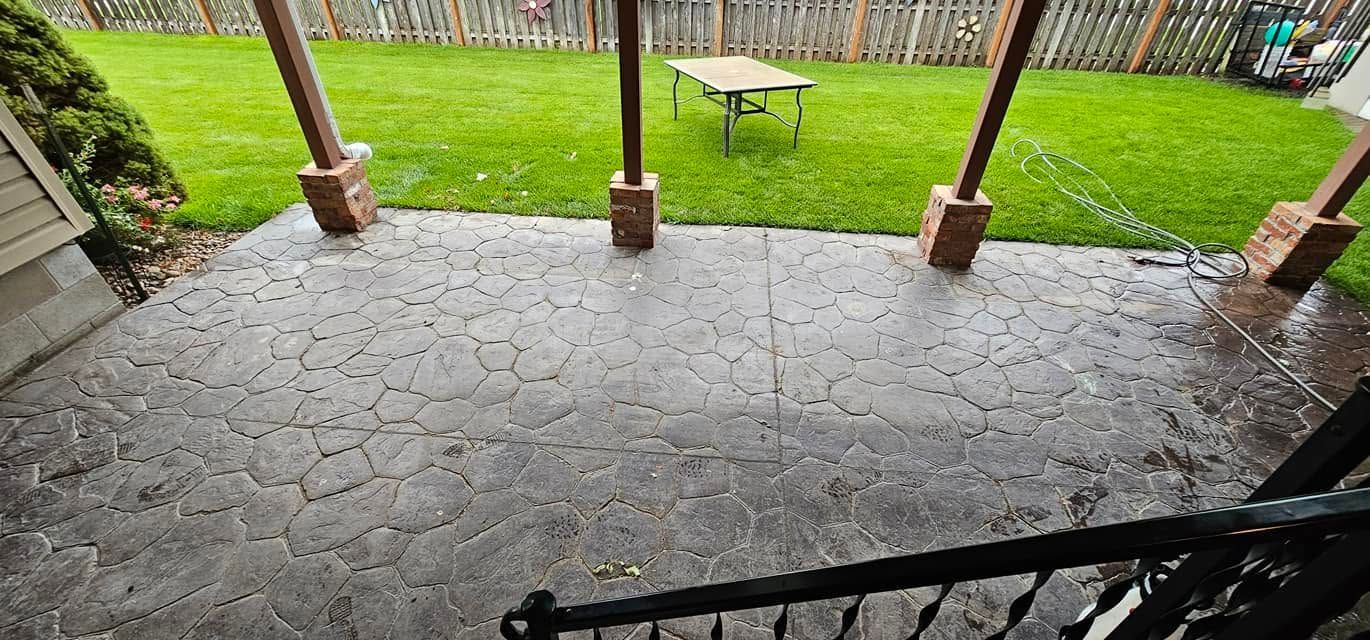 Covered patio with wet stone floor, wooden posts, and a green yard beyond the steps.